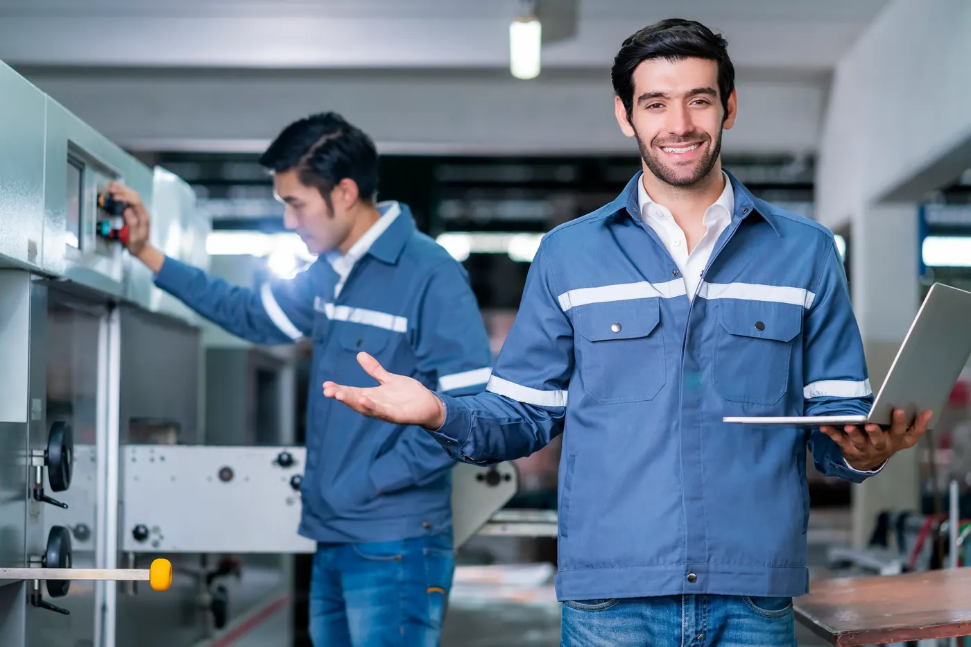 Smiling engineer on a manufacturing floor beside a colleague at a control panel